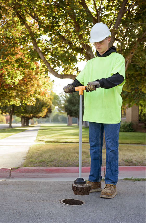 Wide angle street view of utility worker using EZLyft to lift water valve cover — residential street
