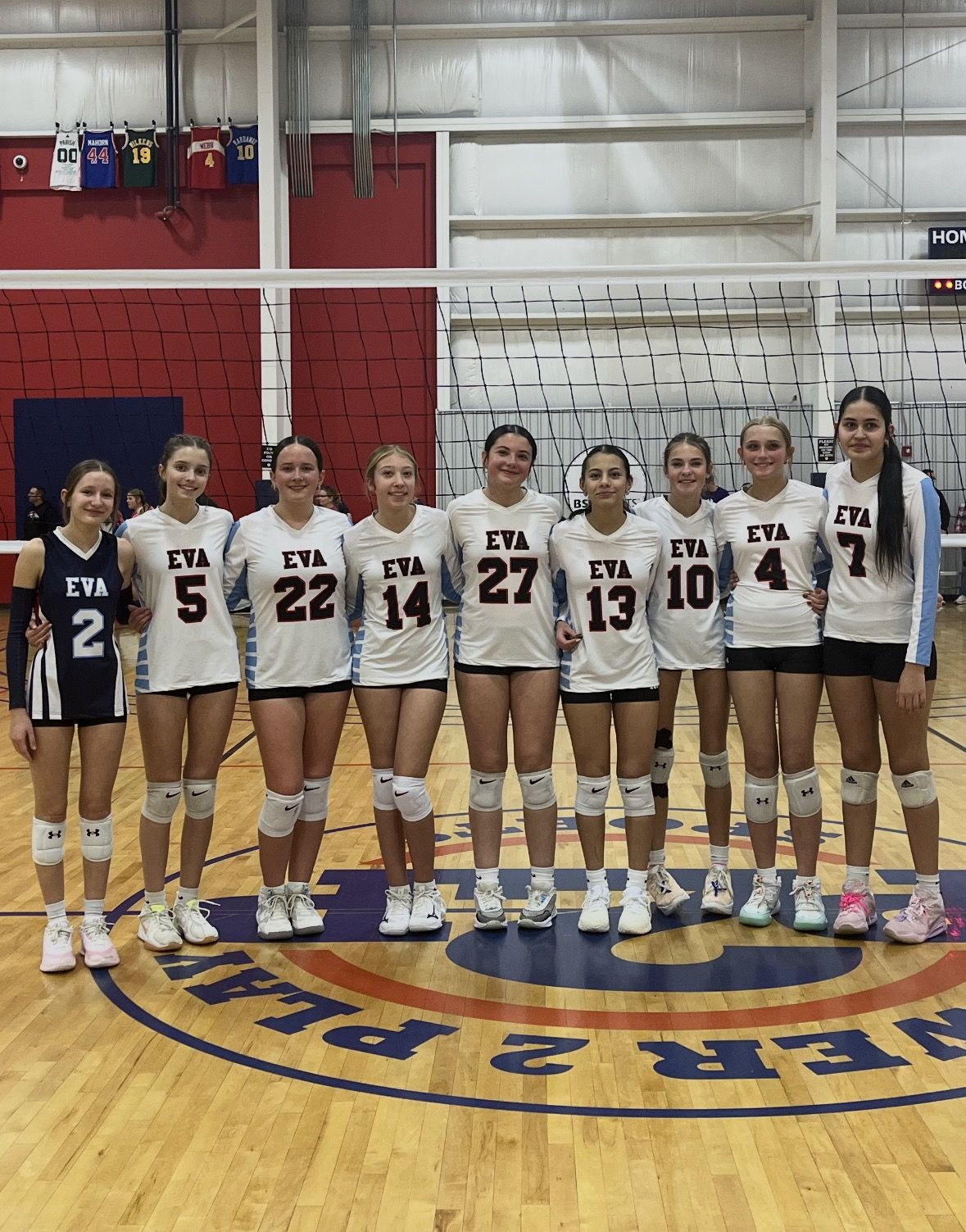 EVA players lined up on a gym floor in white and navy jerseys