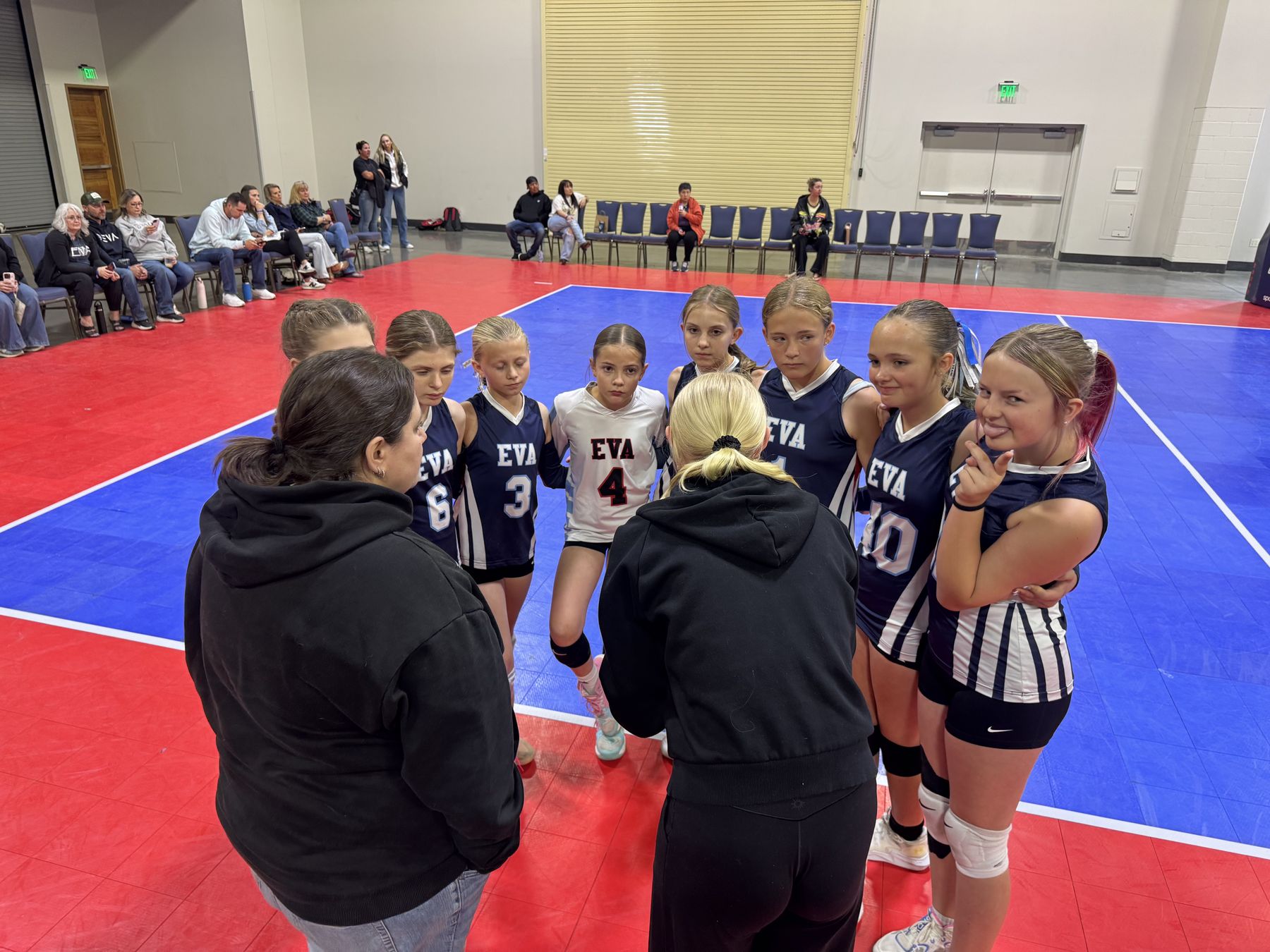 Two EVA coaches huddle with a younger team on a red and blue court