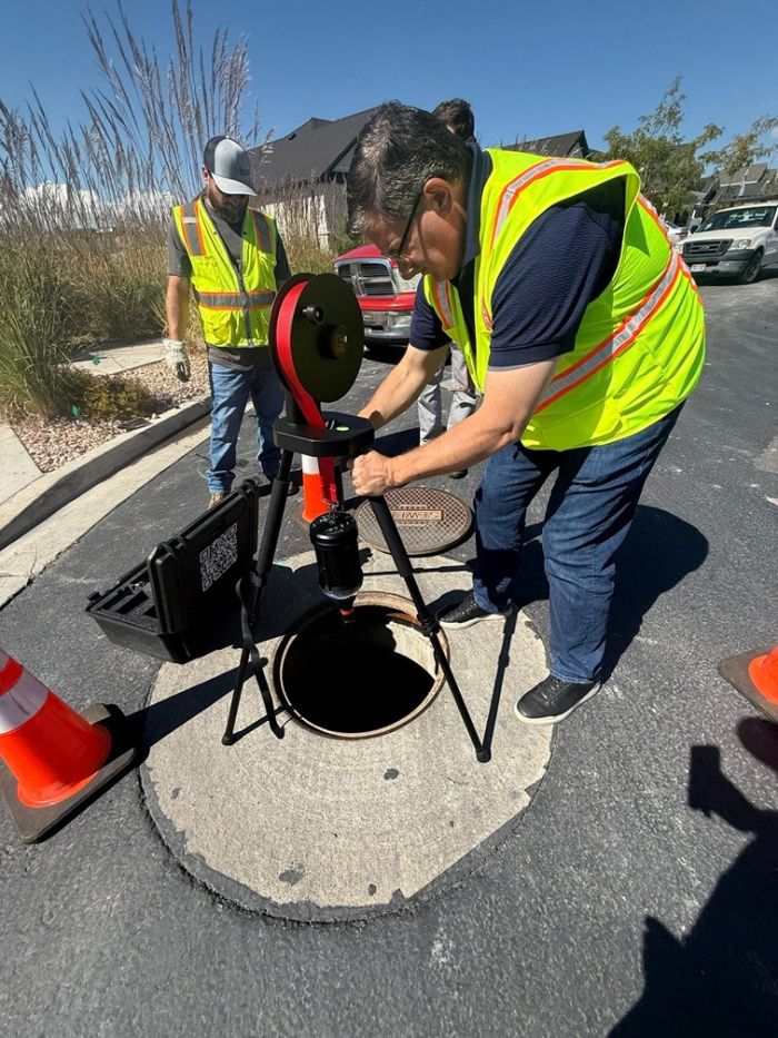 Crew in safety vests running an RV-MAX 360 on a reel tripod over an open manhole during a field demo